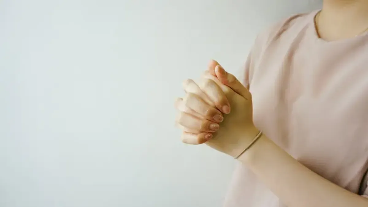 person wearing pink crew-neck shirt with hand clasped together