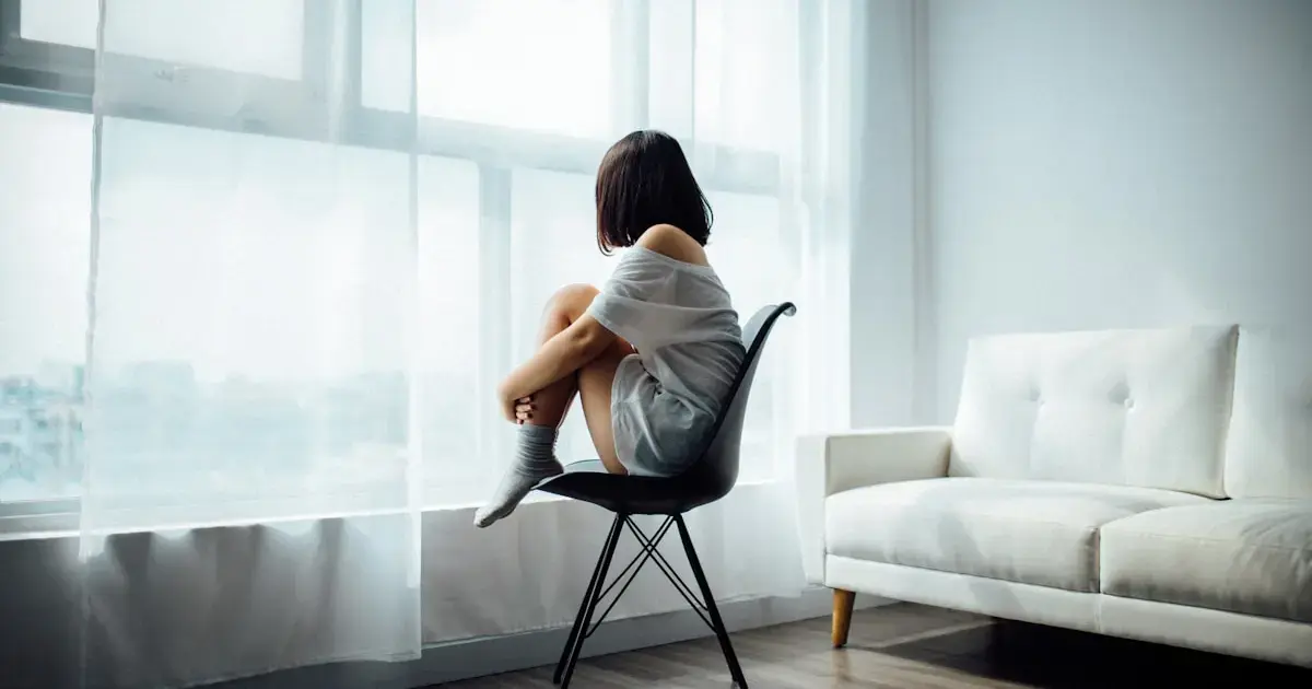 A woman sitting on a chair, hugging her knees