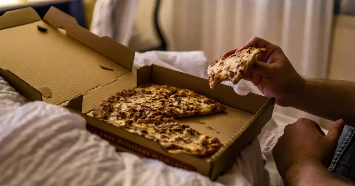 man eating pizza in bed