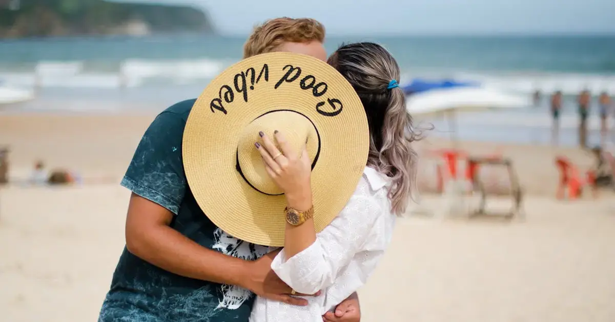 Man and woman on a beach covering their faces with a hat